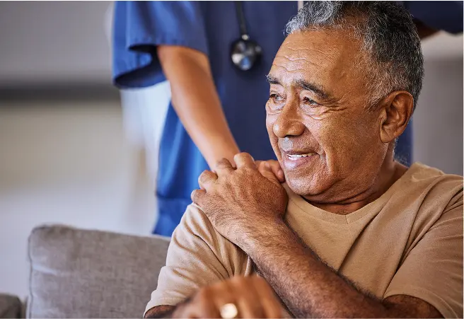 An elderly man smiling while receiving a shoulder massage from a healthcare worker in a blue uniform, in a wellness center setting.