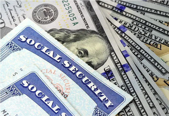 A close-up of various U.S. dollar bills, including Social Security cards and $20 bills, with part of Benjamin Franklin's portrait visible on the $100 bill.